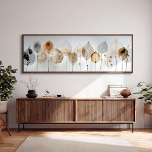 May include: A rectangular framed artwork displaying a series of dried leaves in shades of brown, beige, and green. The leaves are set against a white backdrop, creating a natural, botanical theme. The frame is a dark brown colour.