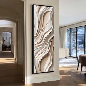 May include: A tall, vertical rectangular wall art piece featuring abstract, flowing, layered waves in shades of cream, beige, and soft white. The artwork is encased in a thin, black frame and displays a smooth, three-dimensional appearance.