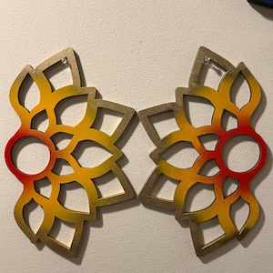 Könnte beinhalten: Zwei dekorative Wandbehänge in Form einer stilisierten Blume. Die Blume ist aus Holz und in Rot-, Orange- und Gelbtönen bemalt. Die Mitte der Blume ist ein Kreis mit rotem Rand.
