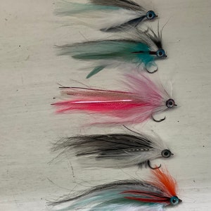 May include: Five different fly fishing lures with various colors and feather patterns. The lures have black hooks and round, blue eyes.