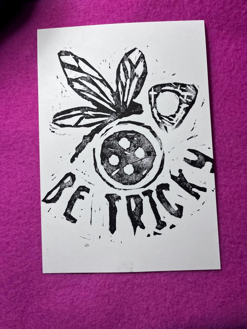 K&ouml;nnte beinhalten: Schwarz-Wei&szlig;-Linolschnitt auf wei&szlig;em Papier. Der Druck zeigt eine stilisierte Libelle, ein kreisf&ouml;rmiges Design mit vier Punkten und das Wort "BE TRICKED" in fetten Buchstaben. Das Kunstwerk ist vor einem magentafarbenen Hintergrund platziert.