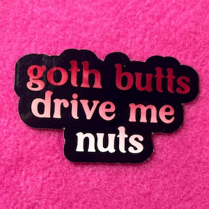 以下が含まれることがあります： 「goth butts drive me nuts」というフレーズが赤と白の文字で書かれた黒いステッカー。ステッカーはピンク色の背景にあります。