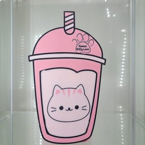 May include: Pink plastic cup with a straw and a cute cartoon cat face. The cup has the text "Kawaii Kitty Love" on it.