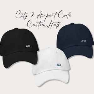 May include: Three baseball caps with different city airport codes embroidered on them. The caps are black, white, and navy blue. The codes are ATL, LAX, and DFW.