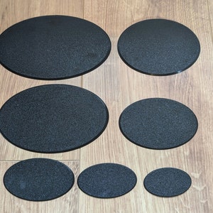 Könnte beinhalten: Eine Sammlung von sieben schwarzen, oval geformten Untersetzern in verschiedenen Größen. Die Untersetzer haben eine strukturierte Oberfläche und sind auf einer hellbraunen Holzoberfläche angeordnet. Sie schützen Oberflächen vor Getränkerändern.