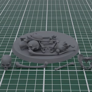 Puede incluir: Un modelo en miniatura gris de restos esqueléticos humanos. El modelo incluye un cráneo, una caja torácica, una pelvis y varios huesos, algunos dispuestos sobre una base circular. Las piezas están dispersas sobre una esterilla de corte verde.