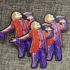 May include: Three colorful stickers featuring a skeleton figure wearing a red and purple glittery outfit, singing into a microphone. The figure has a skull face with a white background.