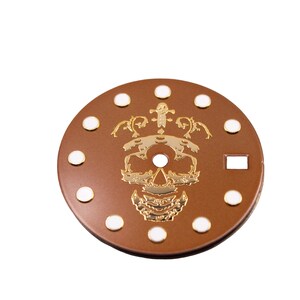 May include: A brown watch face with white dots around the edge and a gold skull design in the center.