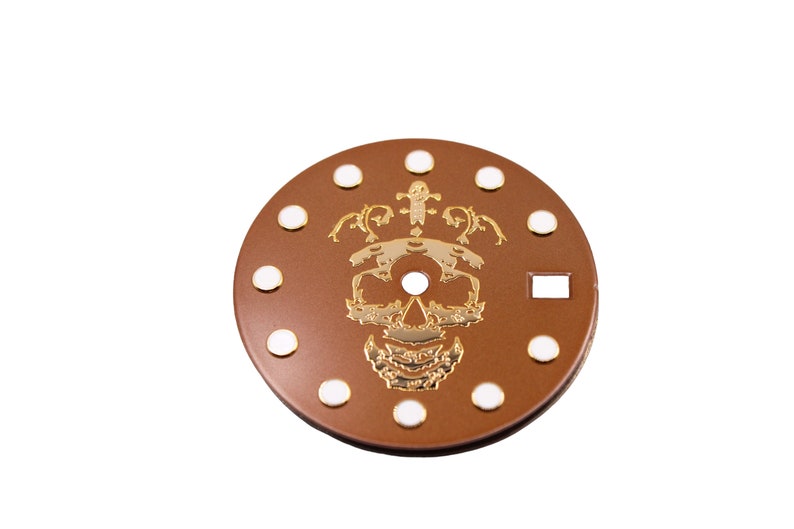 May include: A brown watch face with white dots around the edge and a gold skull design in the center.