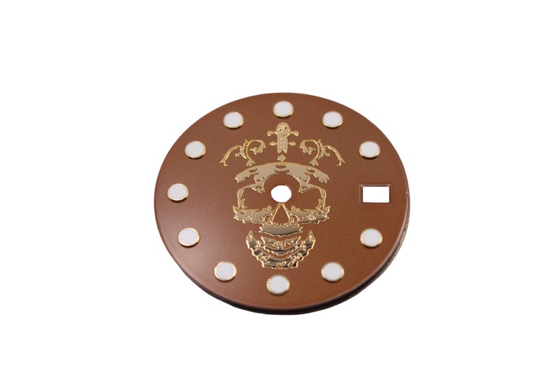 May include: A brown watch face with a gold skull and floral design. The face has white dots around the edge.