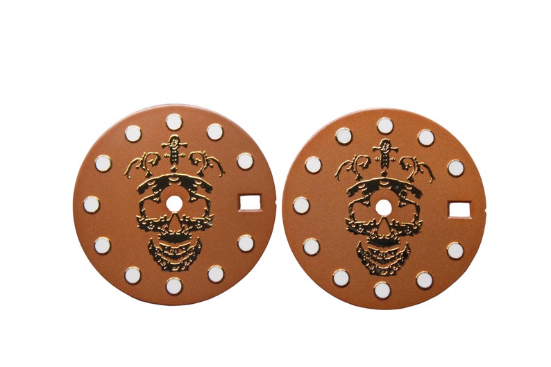 May include: Two round, brown watch faces with white dots around the edge. Each face features a gold skull with a crown and a sword design.