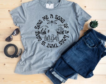 May include: Gray t-shirt with a black circle graphic that says "That is gone sing me a song of a lass". The graphic includes a dragonfly, a mountain range, a ship, and a row of bottles.