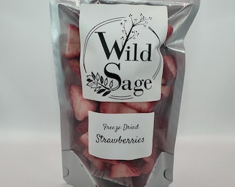 May include: A clear, silver-lined bag filled with freeze-dried strawberries. The bag has a white label with the text "Wild Sage" in a decorative font and a smaller label that reads "Freeze Dried Strawberries". The strawberries are red and appear to be sliced.