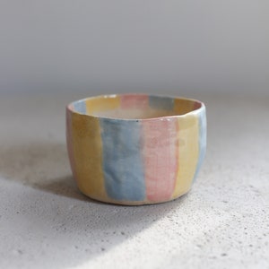 May include: A small ceramic bowl with a striped design in yellow, blue, and pink.
