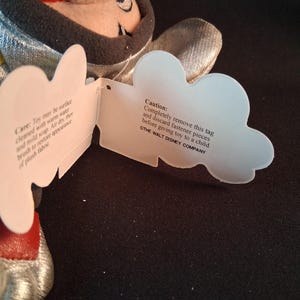 May include: A plush toy with a silver and black design, featuring a red mouth and a tag with care instructions and a caution notice from The Walt Disney Company.