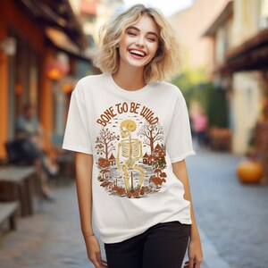 May include: White t-shirt with a graphic of a skeleton sitting in a forest scene. The text "Bone to be wild" is written in a circle around the skeleton.