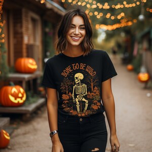 May include: A black t-shirt with a skeleton sitting on a log in a forest scene. The text "Bone to be Wild" is printed on the shirt.