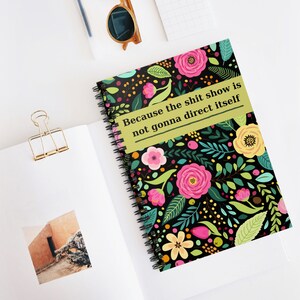 May include: Spiral-bound notebook with a floral design featuring pink and yellow flowers, green leaves, and berries on a black background. The notebook has the text "Because the shit show is not gonna direct itself" in a green rectangle.