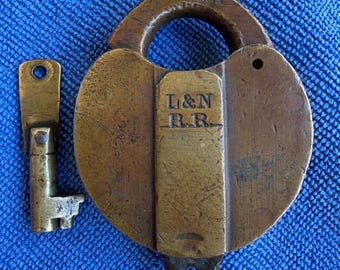 May include: An antique brass padlock and key set. The padlock is round with a curved handle and the text "LOU. KY" is visible. The key is next to the padlock. The padlock has the text "L & N R.R." engraved on it.