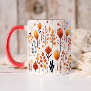 May include: A white ceramic mug with a red handle features a colorful floral pattern in shades of orange, yellow, and brown. The mug is decorated with stylized flowers and leaves.