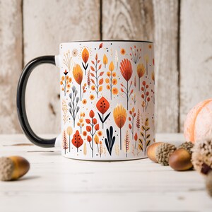 May include: White ceramic mug with a black handle and a black rim. The mug features a pattern of stylized orange, yellow, and red flowers on a white background.