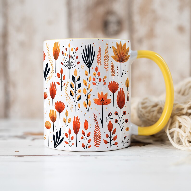 May include: A white ceramic mug with a yellow handle features a colorful floral pattern in shades of orange, yellow, and red. The mug is filled with a floral design of stylized flowers and leaves.