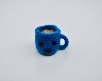 May include: A small blue crocheted coffee mug with a smiling face and brown yarn inside, representing coffee.