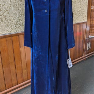 May include: A long, royal blue velvet coat with a collared neckline and button closure. The coat has long sleeves and a flowing silhouette.