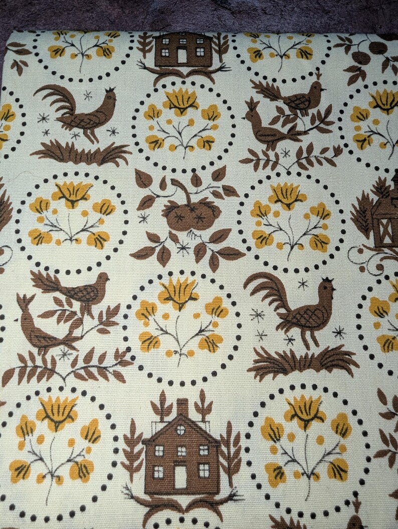 K&ouml;nnte beinhalten: Cremefarbener Stoff mit einem sich wiederholenden Muster aus braunen H&auml;hnen, V&ouml;geln, H&auml;usern und gelben Blumen. Das Design ist in gepunkteten Kreisen eingeschlossen und erzeugt eine Vintage-Bauernhaus-&Auml;sthetik. Der Stoff hat ein strukturiertes Aussehen.