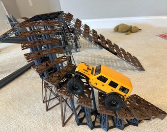 May include: A yellow toy SUV is driving on a brown and grey ramp structure. The ramp has multiple levels and is designed for off-road play. The toy vehicle has black tyres and is positioned mid-climb.
