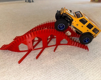 May include: A yellow toy Jeep climbing a red, 3D-printed ramp. The Jeep has black tyres with blue accents. The ramp is made of interconnected, vertical supports. The scene is set on a light-coloured carpet.