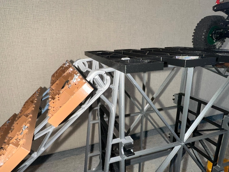 May include: A grey and black plastic structure with a brown ramp. The structure has a grid-like top and is made of multiple connected pieces.