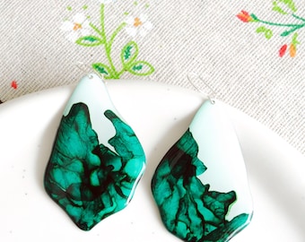 May include: A pair of green and white resin earrings with a unique abstract design. The earrings are teardrop shaped and have a silver hook.