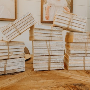 May include: A stack of white books with names written on the spines, tied together with twine. The books are arranged in four stacks on a wooden table.