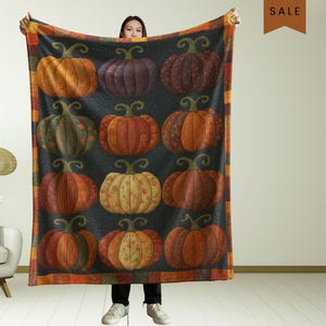 May include: A large, rectangular blanket featuring a repeating pattern of colorful pumpkins in shades of orange, purple, and brown against a dark background. The blanket has a decorative border with orange and brown stripes. The pumpkins have green stems.