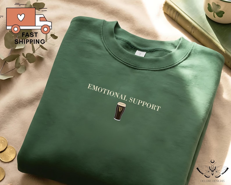 May include: A dark green sweatshirt with the words "EMOTIONAL SUPPORT" printed in white. Below the text is a small graphic of a pint of stout. The sweatshirt is made of a soft material.