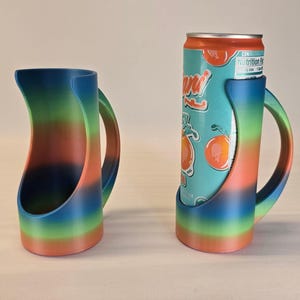 May include: A pair of rainbow-colored can holders. One holder is empty, the other holds a can of Arizona Iced Tea. The holders have a handle and a curved design, with a gradient of colors from blue to green to orange.