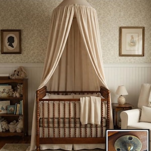 May include: A wooden crib with a spindle design, draped with a beige fabric canopy suspended from a brass ceiling hook. The crib features a matching beige blanket and a plaid bumper pad. An inset shows a close-up of the ornate brass ceiling hook.
