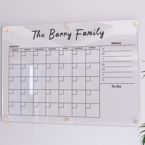 Pode incluir: Um quadro branco de acrílico transparente com uma grade de calendário preta, o título "The Barry Family" e seções para as listas de "Menu" e "To Do".