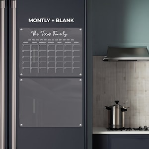May include: A clear acrylic monthly calendar and blank board set, mounted on a dark grey refrigerator. The calendar is labelled "The Texas Family" and includes days of the week and dates. The blank board is below the calendar. The text "MONTLY + BLANK" is at the top.