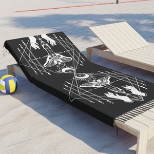 May include: Black beach towel with a white geometric design featuring two butterflies, moons, and hands. The towel has fringe on the edges.