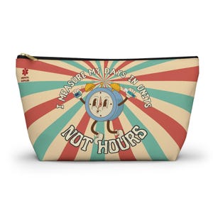 May include: A beige cosmetic bag with a retro design featuring a cartoon clock character. The clock is blue with yellow bells and holds syringes. Text reads "I measure my days in units not hours." The bag has a black zipper.