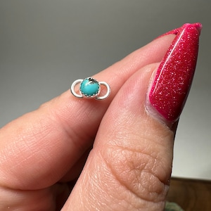 May include: A silver ring with a turquoise stone set in the center. The ring is a simple design with a smooth finish.