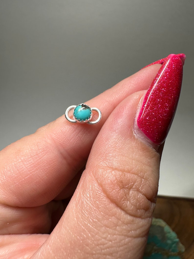 May include: A silver ring with a turquoise stone set in the center. The ring is a simple design with a smooth finish.