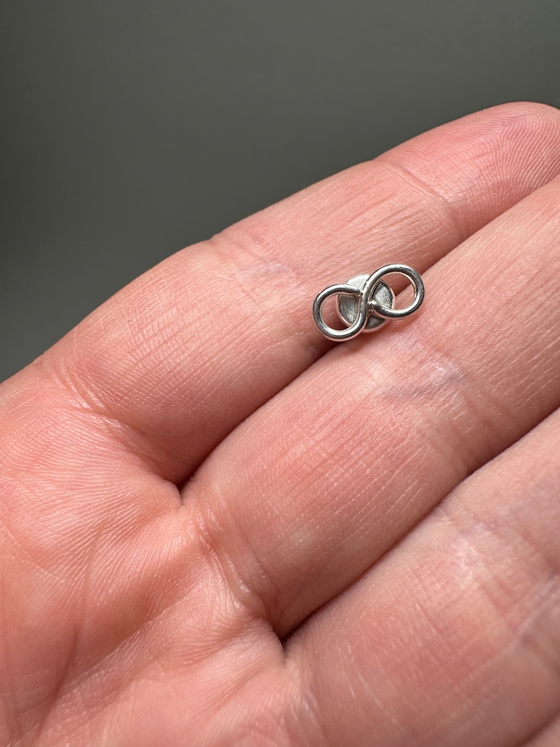 May include: A silver infinity symbol earring. The earring is small and delicate, and it is perfect for everyday wear.