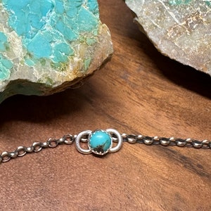 May include: A silver chain bracelet with a turquoise stone set in a silver circle.
