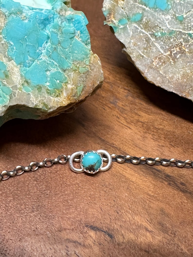 May include: A silver chain bracelet with a turquoise stone set in a silver circle.