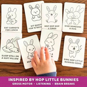 Peut inclure: Un ensemble de cartes blanches avec des dessins au trait noirs de lapins, chacun avec une activit&eacute; diff&eacute;rente. Le texte sur les cartes comprend "Manger des carottes pour le d&eacute;jeuner" et "Faire un c&acirc;lin &agrave; quelqu'un". Une main d'enfant tend la main vers les cartes. Le bas de l'image contient le texte "Inspired by Hop Little Bunnies".