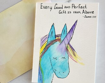 Puede incluir: Una pintura de acuarela de un unicornio azul con un cuerno morado y una crin arcoíris. El texto "Every Good and Perfect Gift is from Above - James 1:17" está escrito debajo del unicornio.