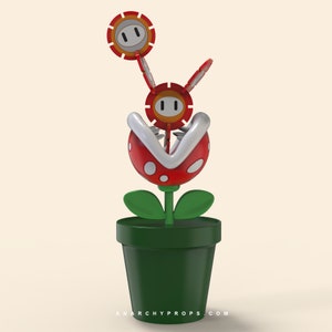Puede incluir: Una planta Piraña impresa en 3D de la serie de videojuegos Super Mario. La planta tiene una cabeza roja con manchas blancas y una boca con borde blanco, hojas verdes y está en una maceta verde oscuro. El texto "ANARCHYPROPS.COM" está en la parte inferior.